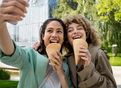Zwei Frauen essen ein Eis in der Parklandschaft und machen dabei ein Selfie