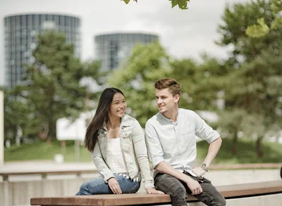 Zwei junge Menschen sitzen im Grünen, im Hintergrund sind die zwei Autotürme der Autostadt zu erkennen