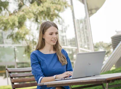 Eine Dame sitzt im Außenbereich an einem Tisch und arbeitet an ihrem Laptop