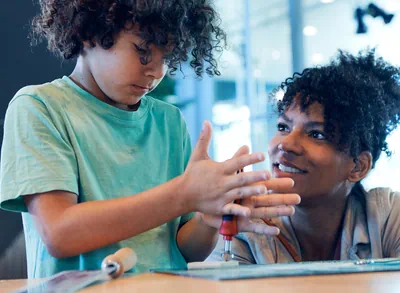 Eine Mutter unterstützt ihren Sohn beim Werkeln an den Werkstationen
