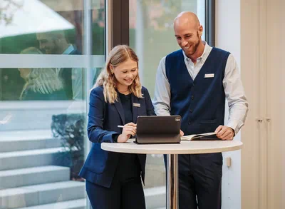 Zwei Mitarbeitende der Autostadt stehen an einem Tisch und schauen auf ein Tablet