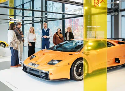 Fünf Gäste und ein Mitarbeiter der Autostadt vor einem orangenem Lamborghini aus dem Jahr 1999