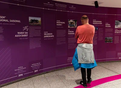 Ein Mann steht vor einer Wand, welche die Chronik der Autostadt zeigt